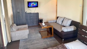 A modern living room with a sofa, armchair, and a coffee table. A TV is mounted on the wall, and there is a cabinet below it.