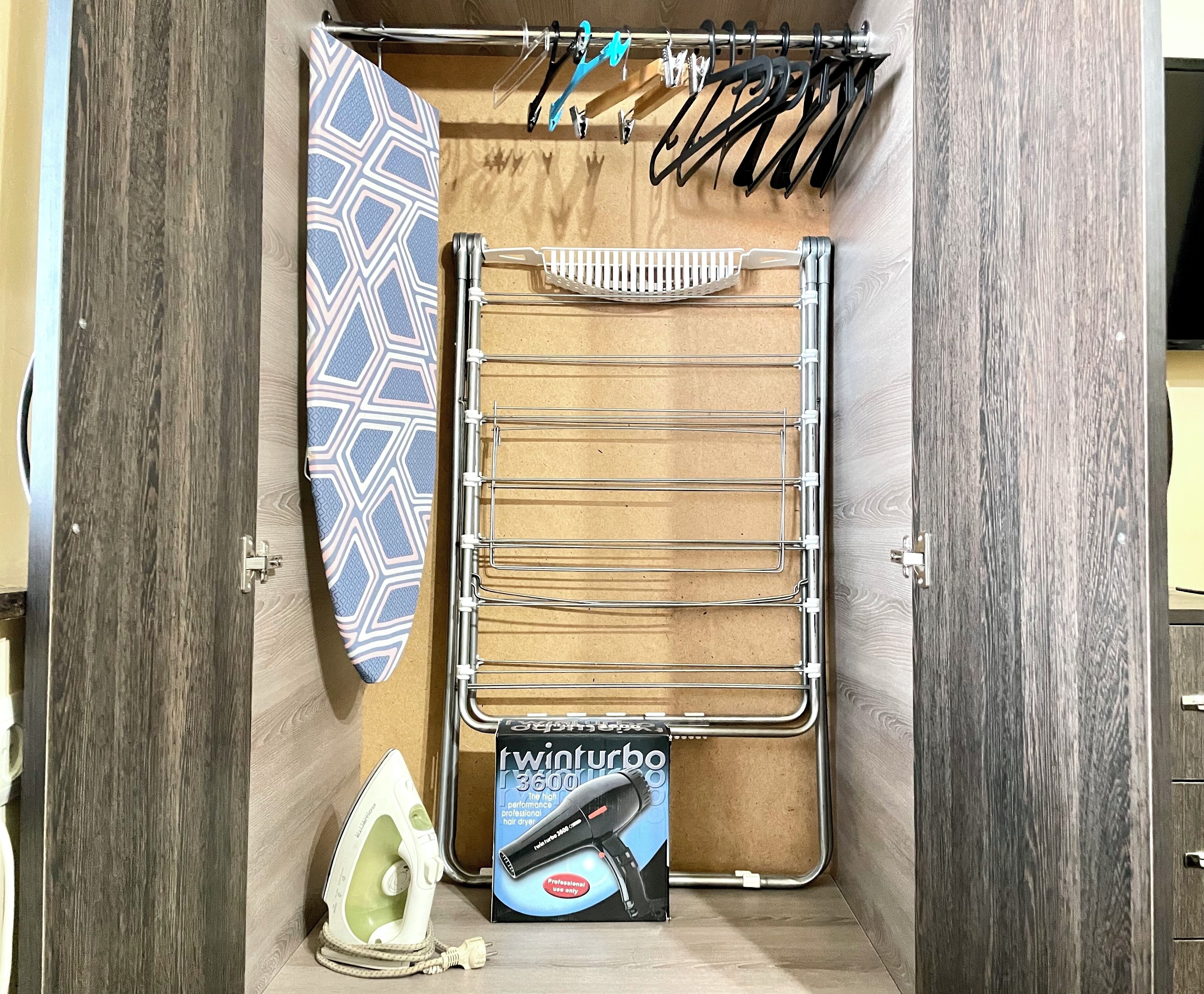Un meuble de rangement compact doté d’une tringle pour suspendre les appareils de coiffure, un sèche-cheveux et un fer à repasser.