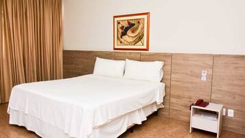 Quarto de hotel com uma cama, mesa de cabeceira, telefone e um quadro na parede.