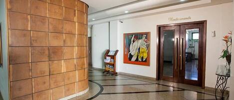 A lobby with a wooden panel wall, a reception desk, a painting, and a door labeled "Restaurante".