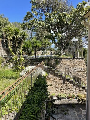 A stone pathway leading to a seating area with a metal fence and potted plants.