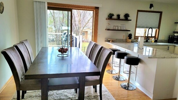 A dining area with a long table and six chairs, a kitchen with a countertop and bar stools, and a sliding glass door leading to an outdoor area. - Clean, Comfy, digs close to all the attractions (Eagan)