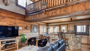 A spacious living room with a large TV, leather sofas, and a stone fireplace.