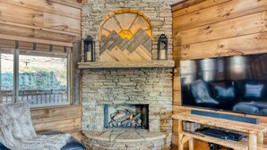 A cozy living room with a stone fireplace, a black leather sofa, and a flat-screen TV.