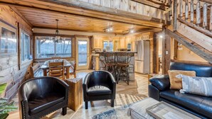 A spacious cabin interior with a dining area, kitchen, and a staircase leading to an upper level.