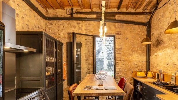 Une cuisine rustique avec une table en bois, un four encastré et une fenêtre donnant sur les arbres.
