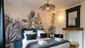 Une chambre avec un grand lit, une table de chevet, un miroir et un mur orné d’une fresque représentant des motifs végétaux.