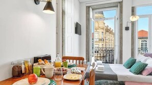 A breakfast setup with a table, breakfast items, and a bed with pillows.