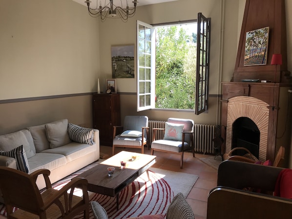A living room with a sofa, chairs, a coffee table, a fireplace, and a large window with a view of greenery.