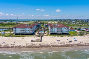 A beachfront hotel with multiple buildings, a pool, and a beach area with umbrellas.