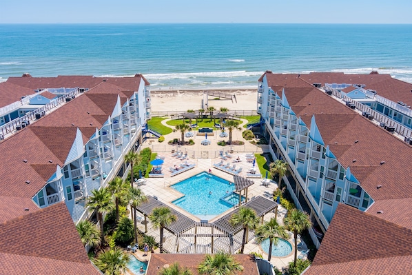 A hotel with a central swimming pool, a beach view, and multiple balconies.