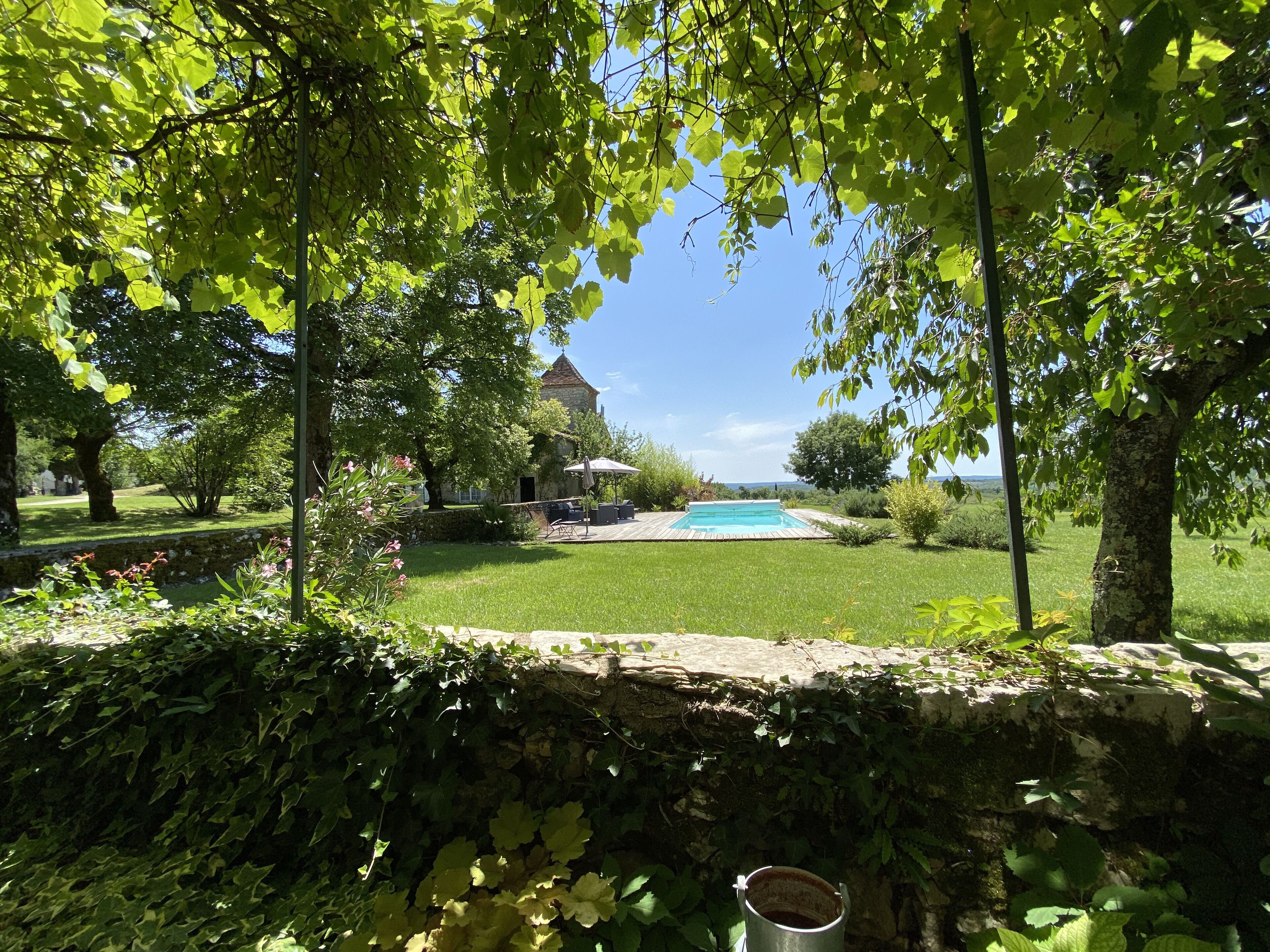 Vue de la piscine et du pigeonnier depuis la tonnelle couverte de vigne vierge.