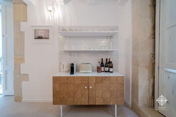 A kitchen with a wooden cabinet, white shelves, and a framed picture. - Casa Tal - Dimora in Ortigia (Syracuse)