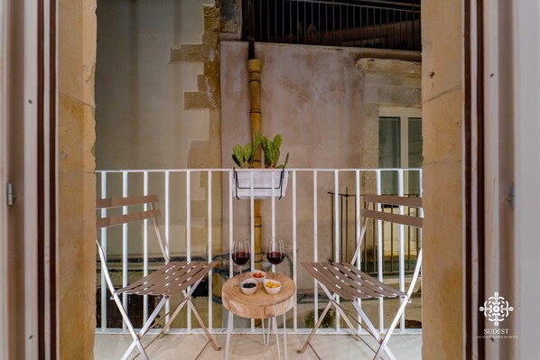 A balcony with a table set for two, featuring a wooden table, two folding chairs, a small plant, and a bowl of fruit.