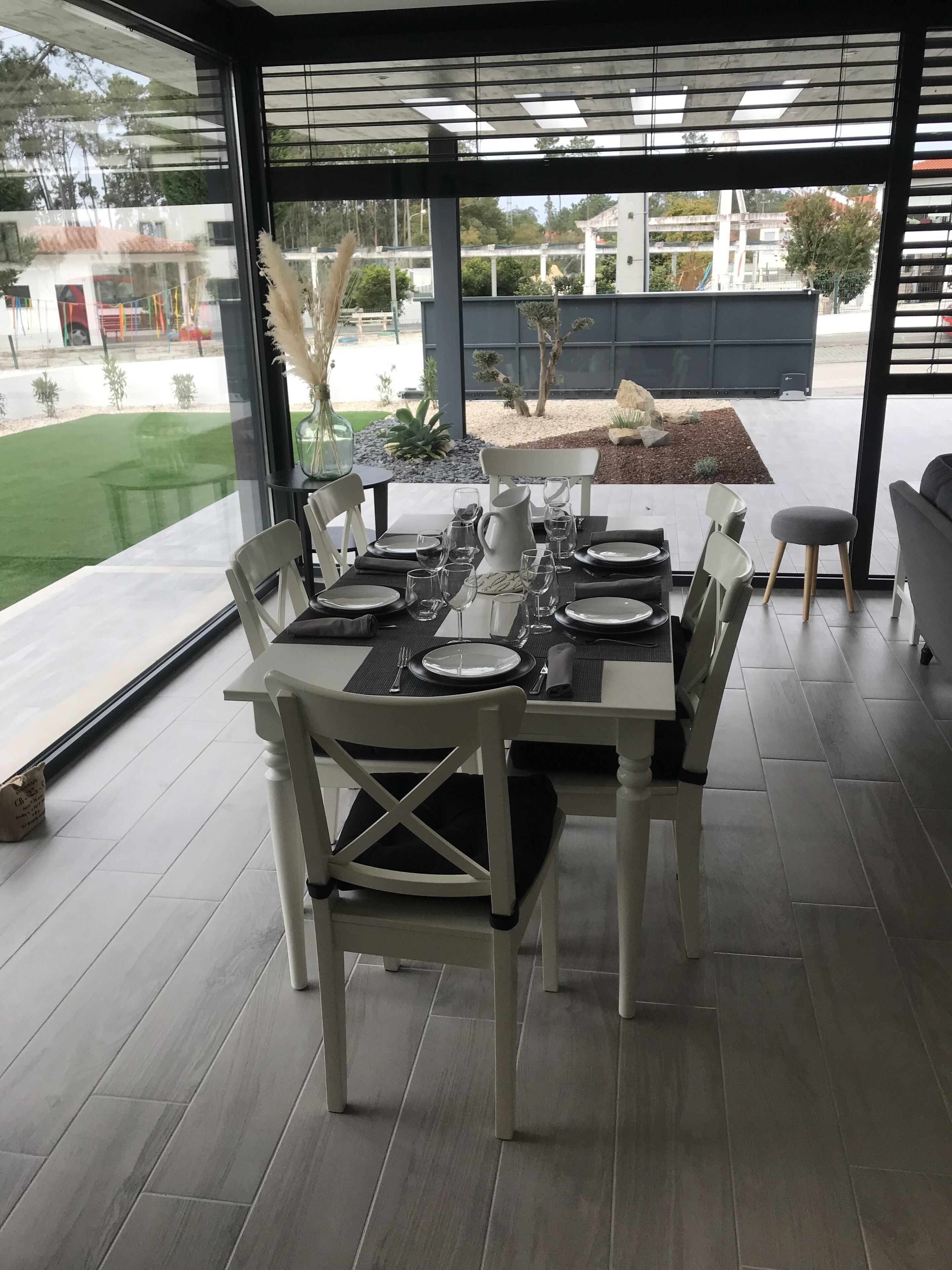 A dining area with a table set for four, large windows, and a view of a landscaped garden.