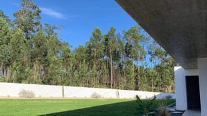 A modern house with a well-maintained lawn, a concrete structure, and tall trees in the background.