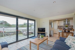 A spacious living room with a large sliding glass door leading to an outdoor patio, a television, a wooden coffee table, and a blue sofa.