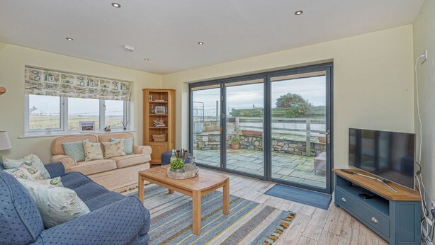 A spacious living room with a large TV, a sofa, a coffee table, and a bookshelf. - Cryd Y Nant -  a bungalow that sleeps 6 guests  in 3 bedrooms (Rhosneigr)