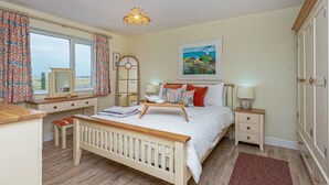 A bedroom with a wooden bed, bedside tables, a dresser, a window with curtains, a mirror, and a painting on the wall. - Cryd Y Nant -  a bungalow that sleeps 6 guests  in 3 bedrooms (Rhosneigr)