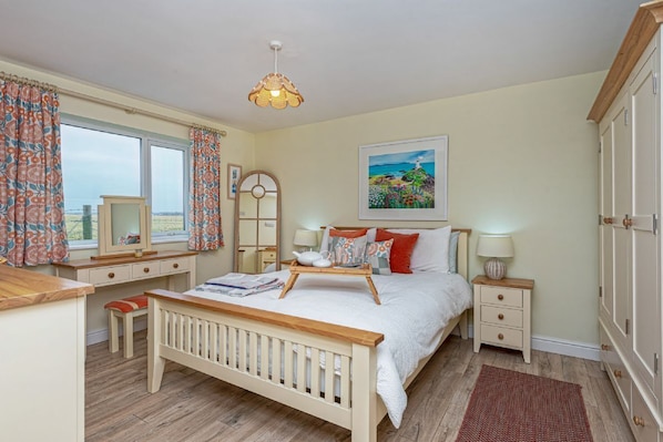 A bedroom with a wooden bed, bedside tables, a dresser, a window with curtains, a mirror, and a painting on the wall.