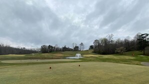 Un campo de golf con un estanque, árboles y cielo nublado.