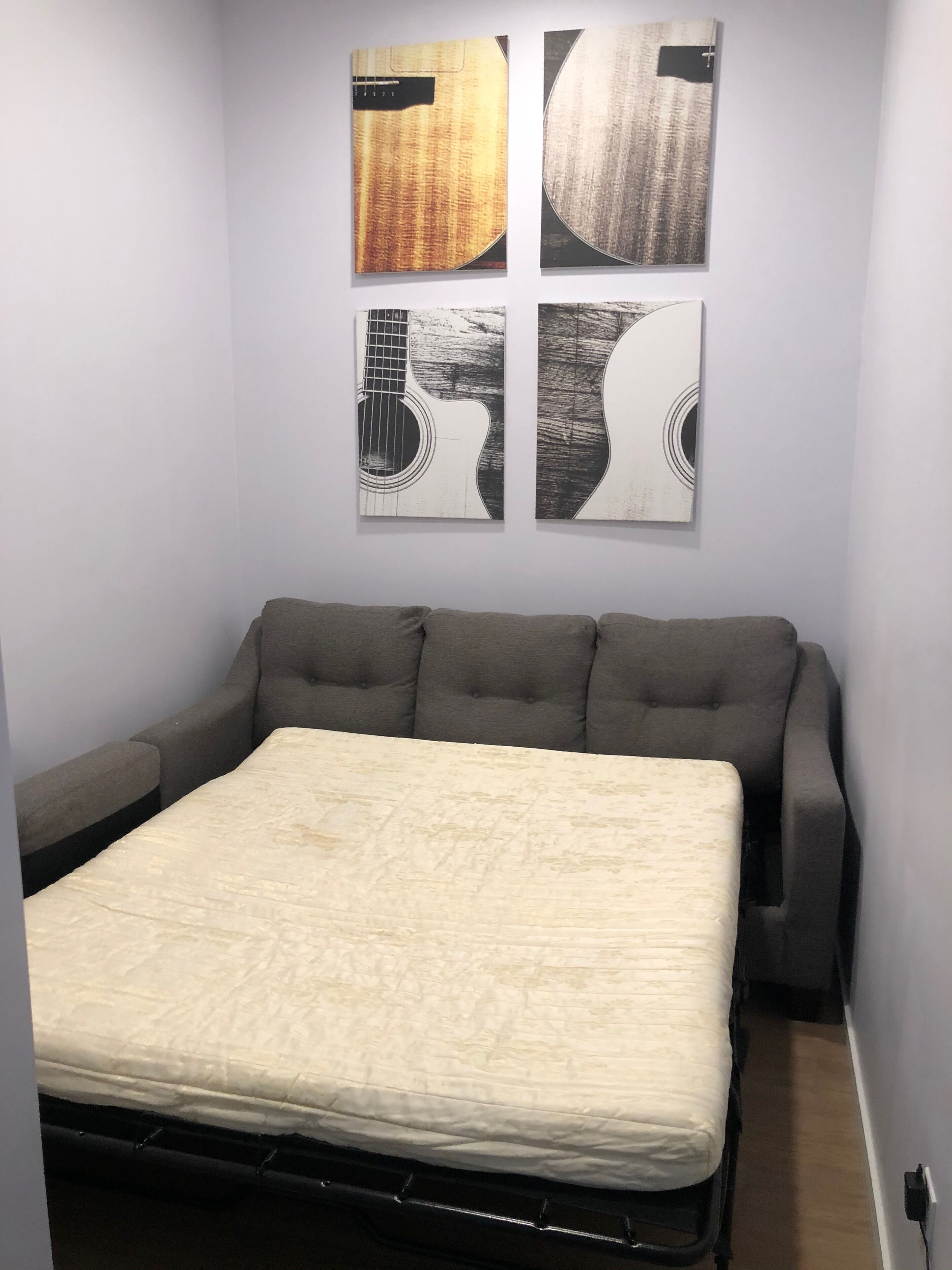 A bedroom with a bed, a gray sofa, and four wall-mounted artworks.