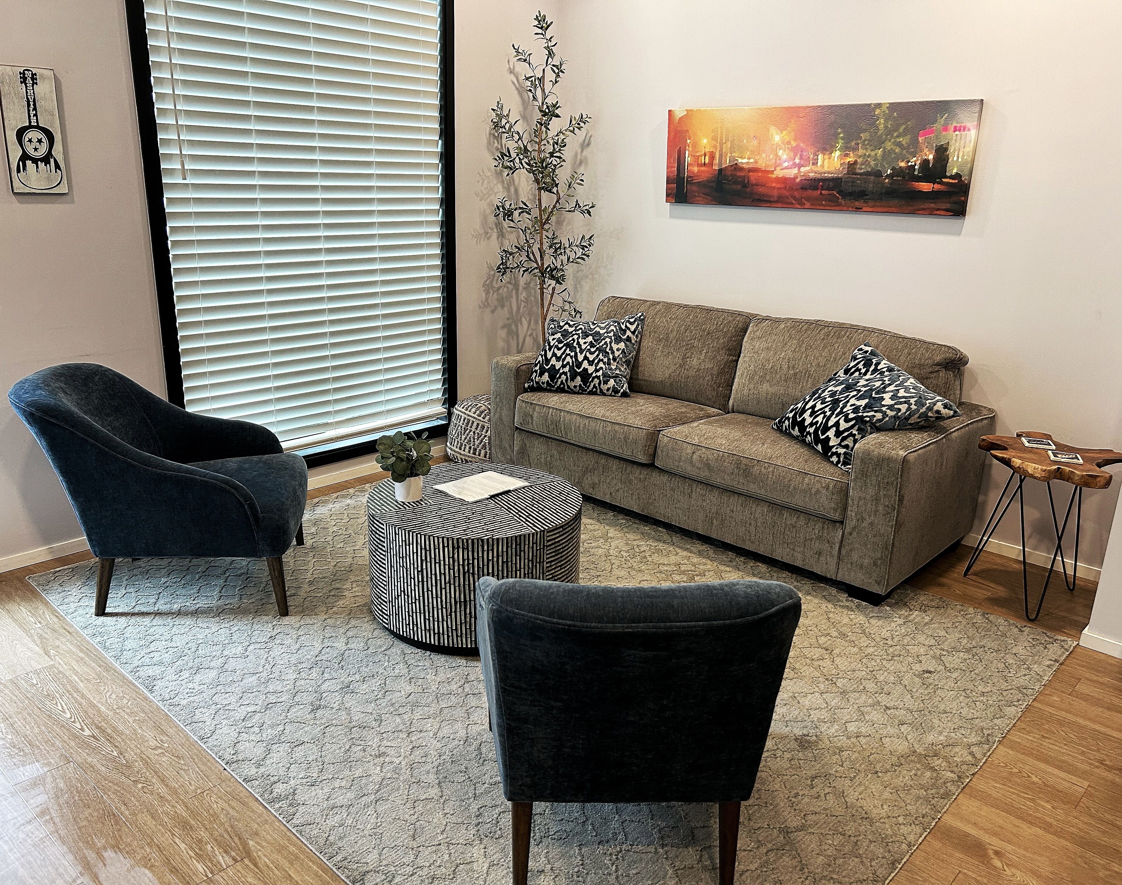 Un salon avec un canapé gris, deux fauteuils, une table basse ronde et un tableau accroché au mur.