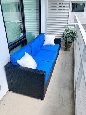 A balcony with a blue sofa, white cushions, and a potted plant. - Downtown Condo! Heated Pool! Walk to the Gulch! Free Parking!  (Nashville)