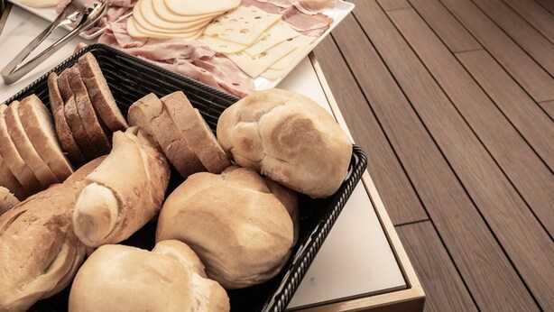 A buffet table with various food items, including bread, cheese, and meats, in a modern dining area with wooden flooring and white chairs. - Relais Manzoni (Rome)