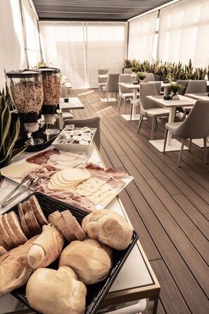 Ein reichhaltiges Buffet mit verschiedenen Speisen, darunter Brot, Käse und Fleisch, in einem modernen Speisebereich mit Holzböden und weißen Stühlen.