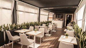 A modern outdoor dining area with wooden flooring, white tables and chairs, and potted plants. - Relais Manzoni (Rome)