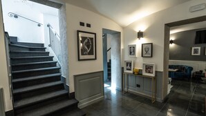 A staircase leading to a landing with framed artwork, a console table with decorative items, and a blue sofa in a modern interior. - Relais Manzoni (Rome)