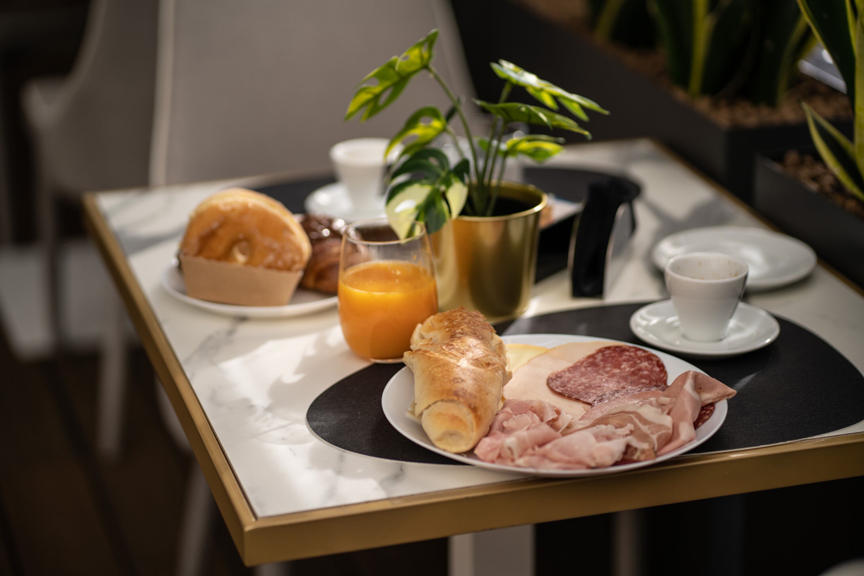 A breakfast tray with croissants, ham, and a glass of orange juice on a marble table.