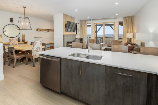 A modern kitchen with a large island, built-in dishwasher, and a dining area with a round table and chairs. - Mountainside Luxury 2-Level Condo at Okemo. Ski-In/Out. (Ludlow)