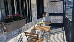 Un balcón con mesa y sillas de madera, plantas en macetas y una pared decorativa con azulejos estampados.