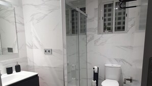 Un baño moderno con cabina de ducha de vidrio, inodoro blanco y tocador negro.