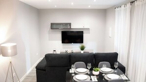Un comedor moderno con un sofá negro, una mesa de vidrio para cuatro personas y un televisor de pantalla plana montado sobre la mesa.