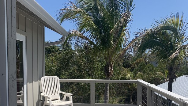 A wooden deck with a white chair and a small table, surrounded by a white railing and palm trees. - Beautiful Bokeelia!!!! Fishing dream! Bring your boat and your dog (Bokeelia)