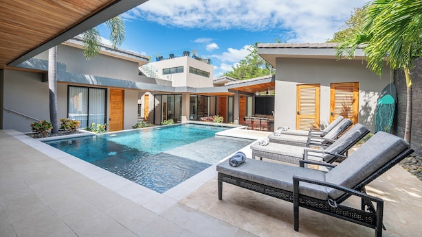 Un área de piscina moderna con sillones de descanso y un porche cubierto.