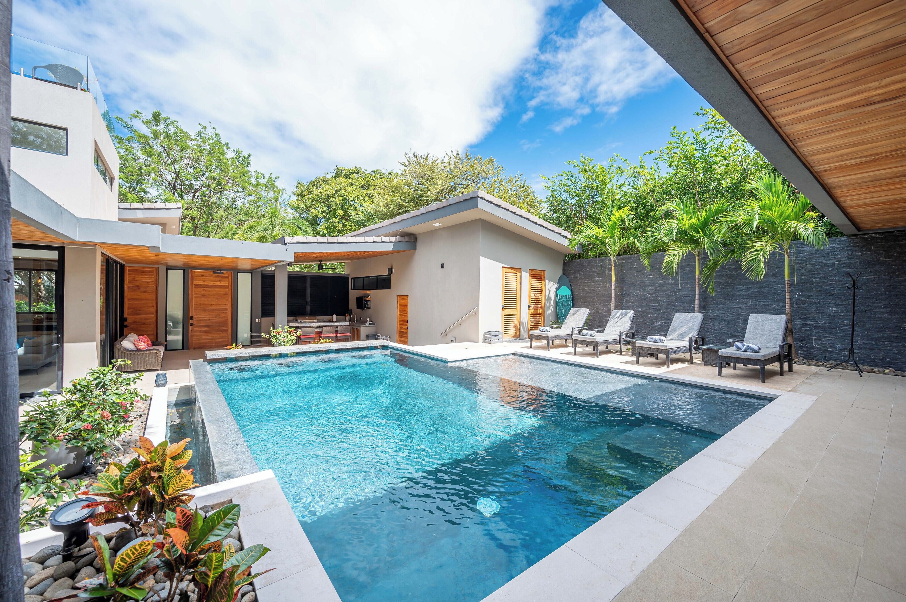 Un espace piscine moderne comprenant une piscine rectangulaire, des chaises longues et un coin repas équipé d’un téléviseur.