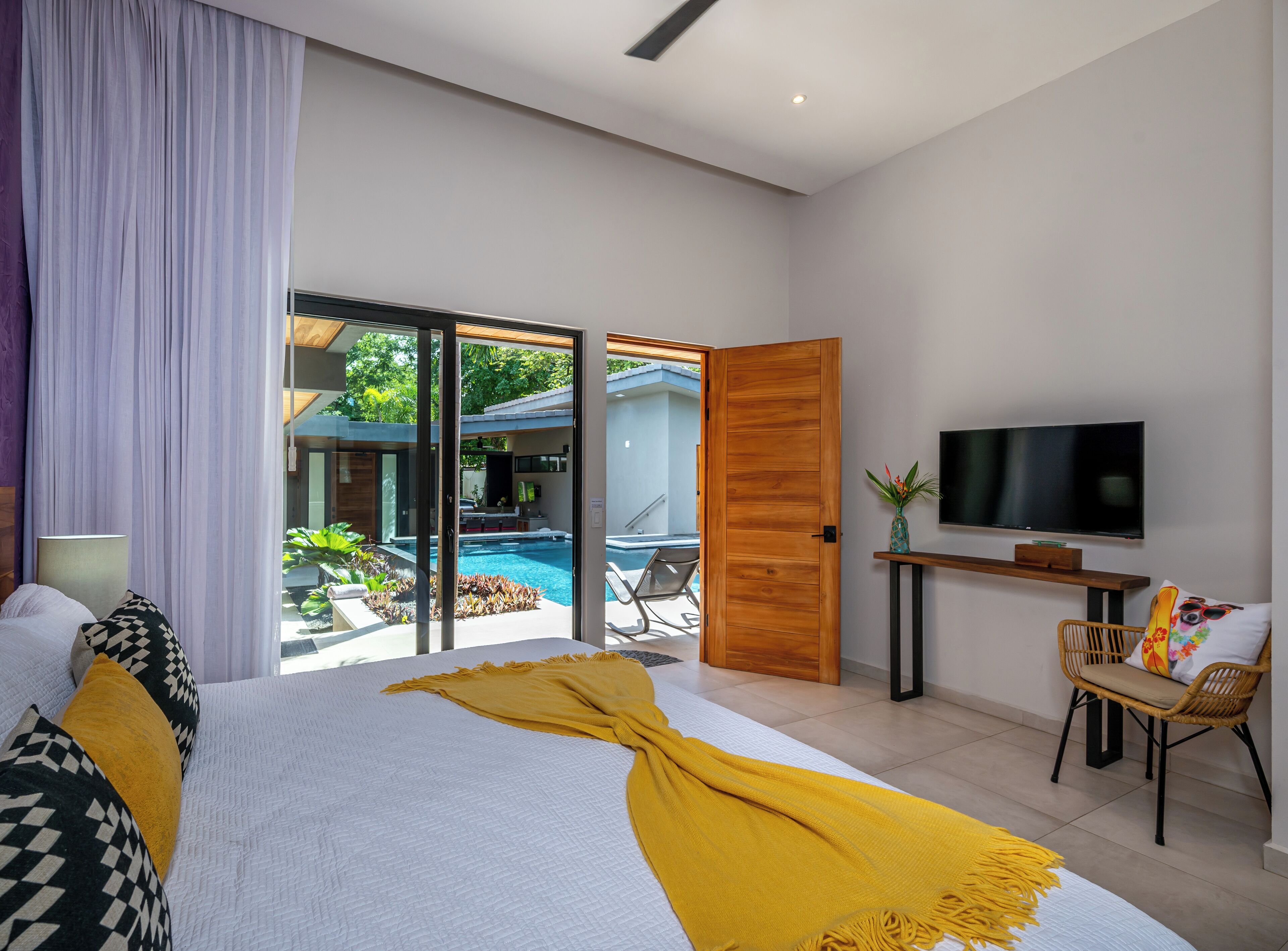 Un dormitorio moderno con una cama grande, un televisor y vistas a una piscina al aire libre.