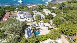 Vista aérea de una zona residencial costera con casas, una piscina y paneles solares.