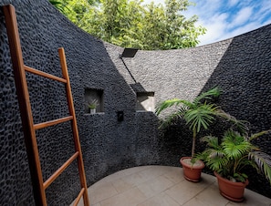 Un espacio exterior moderno con pared texturizada, una escalera de madera, plantas en macetas y suelo de baldosas.