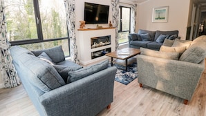 A modern living room with a fireplace, two sofas, a coffee table, and large windows with curtains. - Mayflower (Lifton)