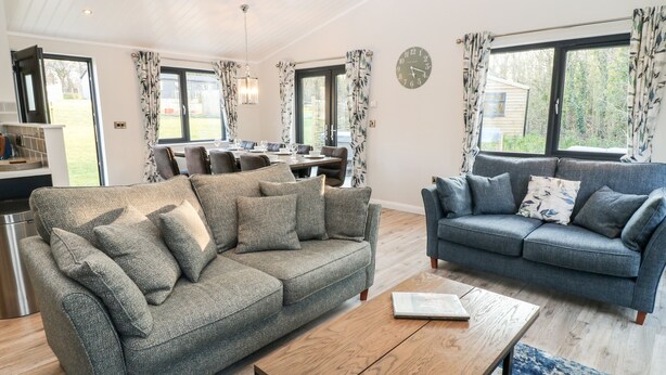 A modern living room with a grey sofa, a blue sofa, and a wooden coffee table. There is a dining area with a table and chairs in the background. - Mayflower (Lifton)