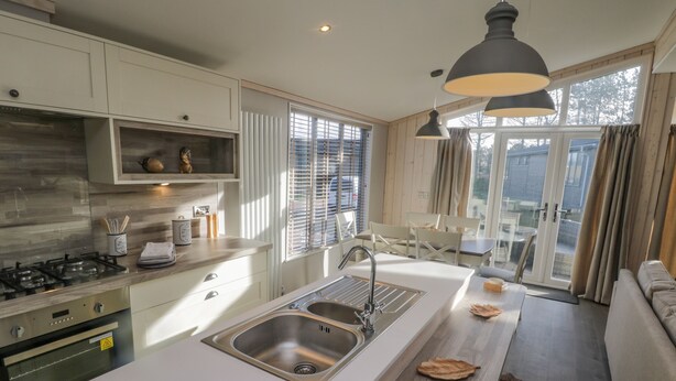 A modern kitchen with a central island, stainless steel sink, and a dining area with a view.