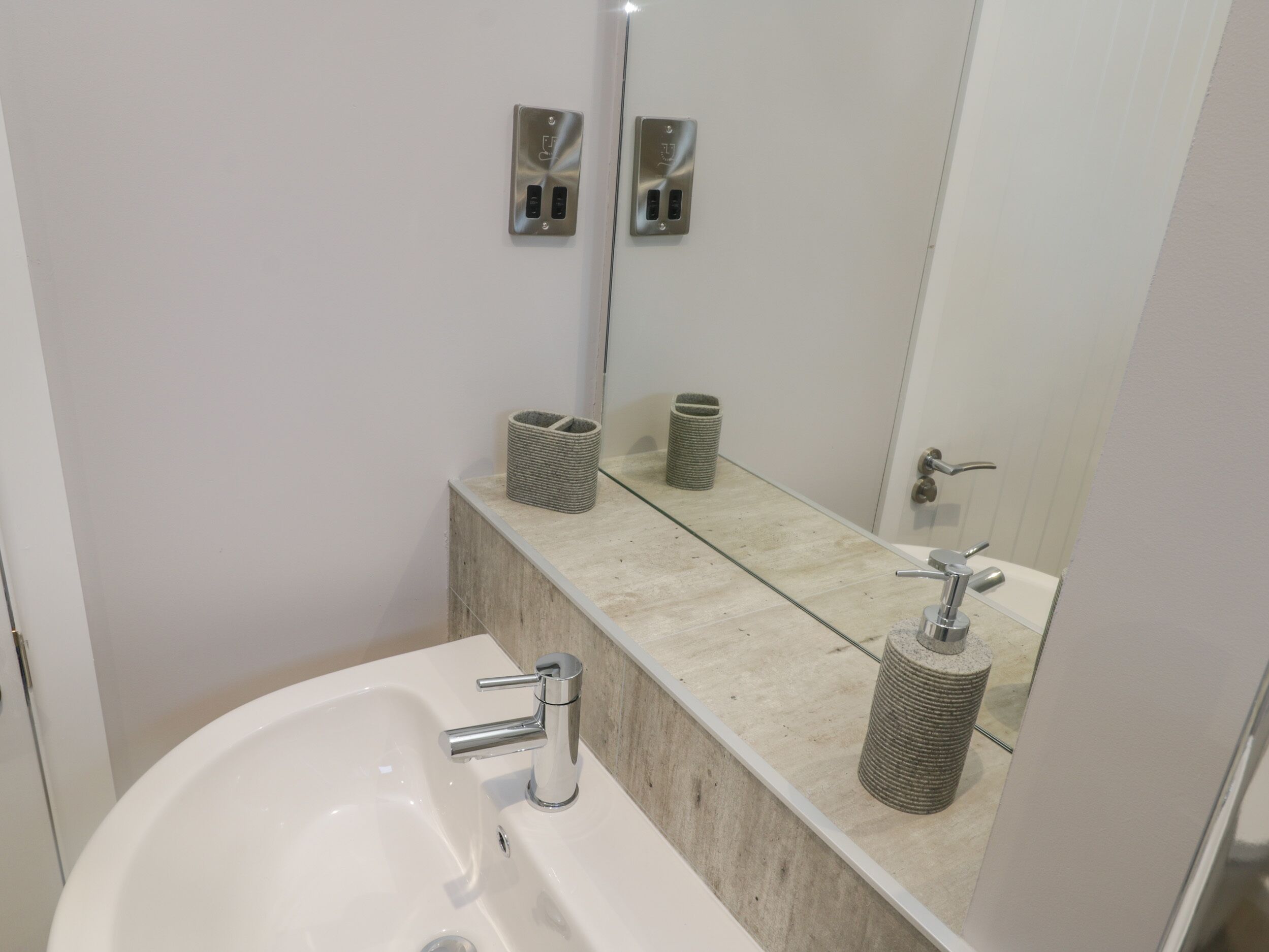 Ein modernes Badezimmer mit einem weißen Waschbecken, einem Spiegel und zwei Händetuchspendern an der Wand.