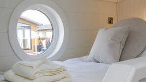 A bed with a round window, a stack of towels, and a pillow.