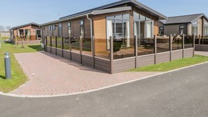 A modern caravan with a large glass window, a brick pathway, and a grassy area.
