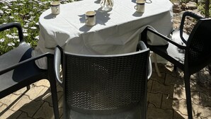 An outdoor table set with a vase of flowers, a teapot, and cups, surrounded by chairs, with a view of trees and a distant landscape. - Gîte 2/4 people with swimming pool and view of the Orb valley (Cessenon sur Orb)